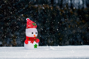 Naklejka na ściany i meble Toy snowman in the woods on a dark background during a snowfall