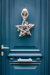 A star-shape Christmas decoration hanging on a blue front door with moldings