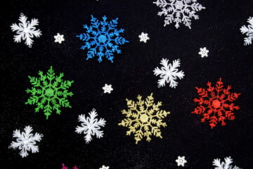Different colors and different sizes of snowflakes lie on a black background.Abstract texture.