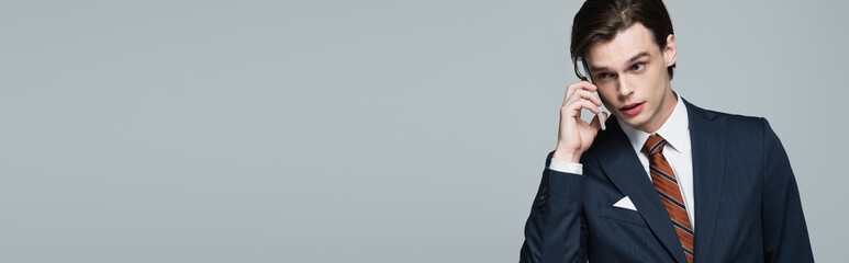 young businessman in suit talking on smartphone isolated on grey, banner