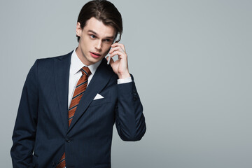 young businessman in suit talking on smartphone isolated on grey