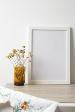 Wooden frame mockup on table with home interior decor elements. White wall background.