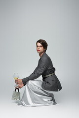 full length of transgender man in slip dress with blazer holding purse and glass of wine while...