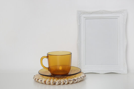 White wooden frame mockup and yellow tea cup on the table.