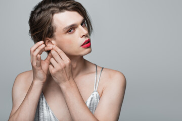 young transgender person touching ear isolated on grey - obrazy, fototapety, plakaty