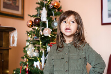 Cute girl child of five or six year old reciting the Christmas poem in the living room in front of the christmas tree - Childhood and Christmas holidays concept