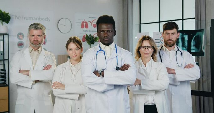 Close up portrait of attractive confident experienced multiethnic medical team which posing on camera with crossed arms in modern hospital workroom