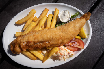 Fresh cooked fried fish fillet with salad and potatoes on a white plate. Fish and chips healthy...
