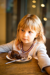 Cute little girl 5 years old blonde eating a cake in a cafe