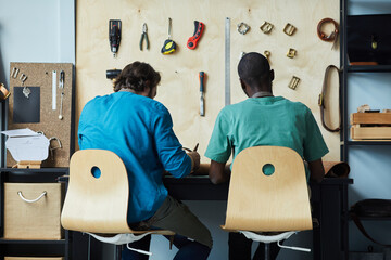 Back view portrait of two male artisans working while sitting by desk in leatherworkers workshop,...