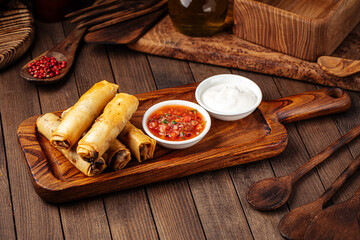 Spring rolls with salsa sauce and sour cream on the wooden background