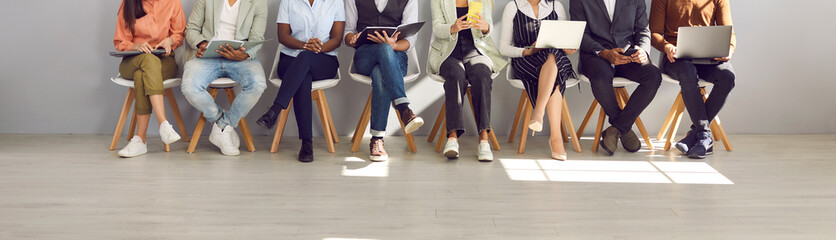 Fototapeta na wymiar Diverse people in smart casual clothes holding paper documents, CVs, resumes, laptops and cellphones waiting in line for job interviews or business appointments in recruitment agency, legs low section