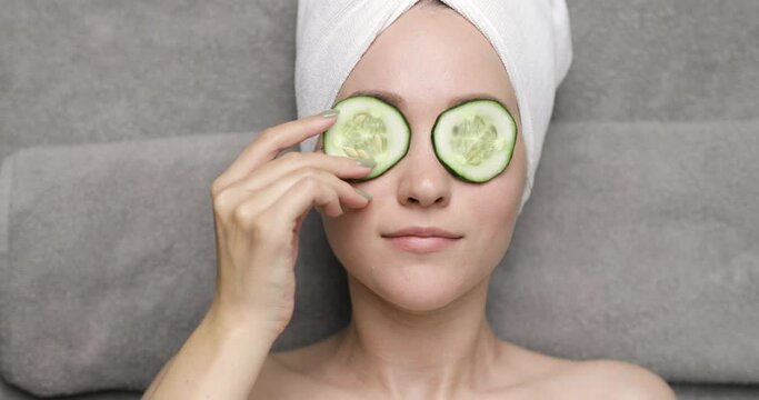 Portrait of a charming young european woman with a white towel on her head,who puts two slices of cucumber over her eyes