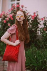 Young beautiful red-haired long-haired woman in a summer pink dress walks through the streets of a summer city.
