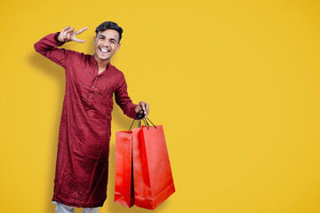 Indian man in ethnic wear with shopping bags, isolated over yellow background