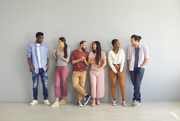 Diverse people leaning on studio background and talking. Full body length indoor group shot of happy young men and women making friends, sharing and listening to opinions and finding common grounds - Powered by Adobe