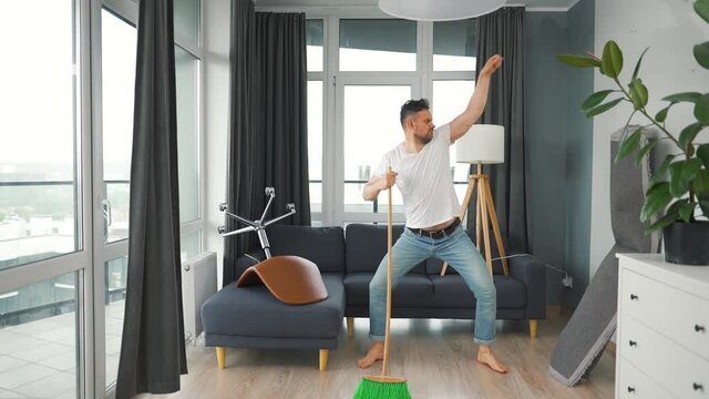 Man cleaning the house and having fun dancing with a broom. Slow motion