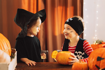 Girl in witch costume and boy in pirate costume looking into pumpkin.
