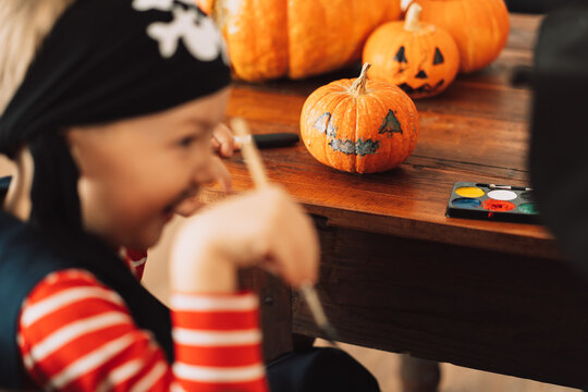Boy dressed as pirate paints face on pumpkin.