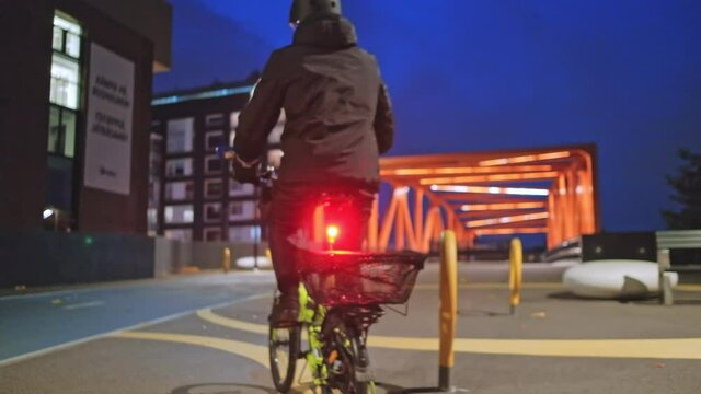The man gets on the bike and leaves at night. The bike has a red light on. Safe cycling concept at night
