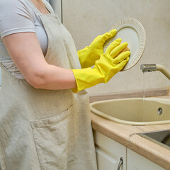 A woman washes a plate with a sponge in the sink while cleaning the home kitchen, close-up