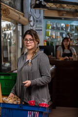 Chica joven comprando en local de productos naturales y detrás del mostrador en la caja se encuentra la empleada de la tienda