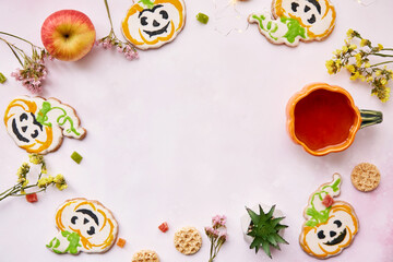 Halloween creative concept background: pumpkin cup and cookies in shape of cute pumpkins. Copy space.Atmospheric aesthetic autumn mood or trick or treat concept. Apples, dry flowers and candied fruit