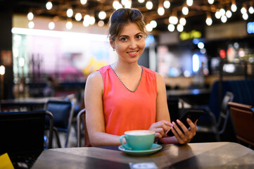 Young woman using her smartphone to browse web content and sending messages while taking a coffee in a bar