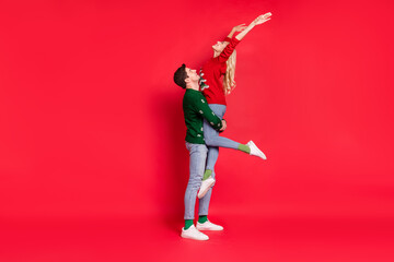 Full length body size photo boyfriend keeping overjoyed happy girlfriend wearing xmas outfits isolated vivid red color background