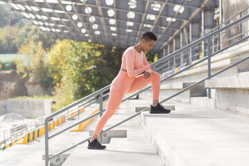 Female athlete doing fitness in a pink sports suit near the sports stadium, African American performs fitness exercises and stretching in the morning