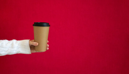 A woman in a white sweater holds a paper cup for coffee, on a red background