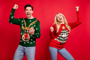 Photo of astonished couple celebrate victory scream goal raise fists wear ugly sweater isolated red...