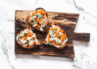 Delicious appetizer, tapas - roasted pumpkin, gorgonzola, honey, thyme bruschetta on a rustic cutting board on a light background, top view - obrazy, fototapety, plakaty