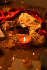 Aroma candle burns on a warm woolen scarf, a knitted sweater and craft letters on the bed. Cozy concept
