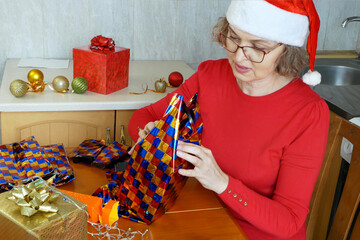 Woman preparing gifts for Christmas and New Year at home in kitchen, smiling woman in santa helper...