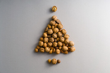 Brazilian nuts, walnuts, almonds shaped as Christmas tree with star and base on Winter and Christmas grey background