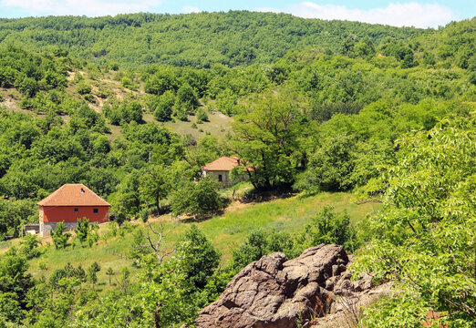 Old and new house next to a large stone with lots of greenery around