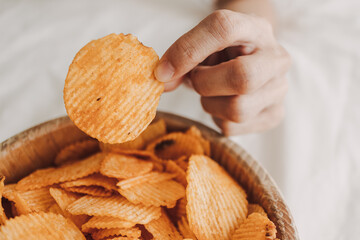 Bowl of potato chips on white sheet bed with hand picking up.