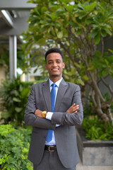 Portrait of handsome African businessman wearing suit and tie while smiling at rooftop park