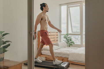 Asian man exercise by walking on the treadmill in his apartment.