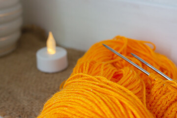 Orange yarn with knitting needles and small candle. Cozy home mood. Autumn concept. Bright orange...