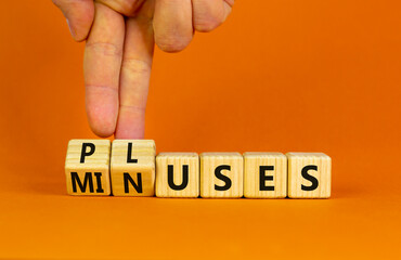 Pluses and minuses symbol. Businessman turns wooden cubes and changes the word 'minuses' to 'pluses'. Beautiful orange table, orange background. Business, pluses and minuses concept, copy space.
