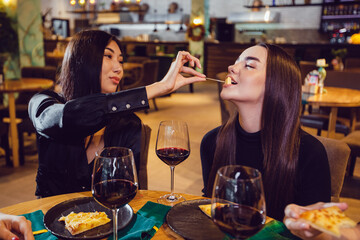Girl feeding her friend cheese in a restaurant.
