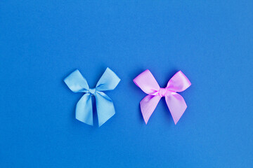 Tied pink and blue bows in the center of  the blue background. Top view. Copy space. Holiday background.