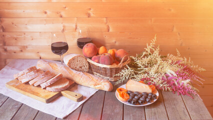 Rustic still life with fruits in wicker basket,  glasses of red wine, bread, cheese, black olives and astilbe flowers.