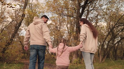 mom dad and child walk along the forest autumn road, happy family life, yellow dry leaves, fallen leaves in the outdoor nature park, father mother and kid walk, girl with parents together.