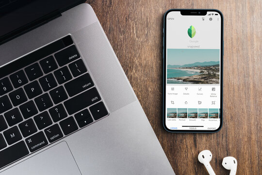 Google Snapseed Mobile app on the smartphone screen on wooden background with a computer beside it. Rio de Janeiro, RJ, Brazil. October 2021.