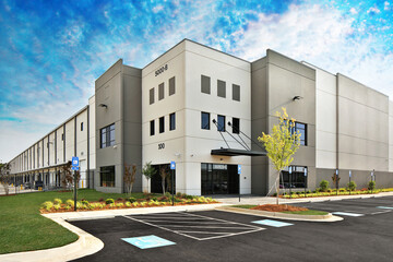 Modern gray warehouse distribution facility and parking lot under gorgeous blue cloudy sky