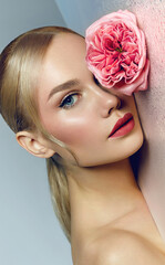 Portrait of a beautiful young woman with perfect smooth skin and blond hair. Woman holding pink flower in her hands. Cosmetics advertising concept. Natural composition. Face and body skin care.