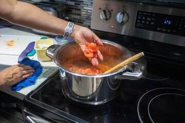 hand of a woman adding chopped tomatoes in a pot. preparing food in a kitchen